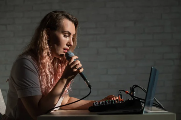 Eine Frau singt in ein Mikrofon und spielt online. Eine Bloggerin nimmt einen Song mit einem Synthesizer und einem Laptop auf. — Stockfoto