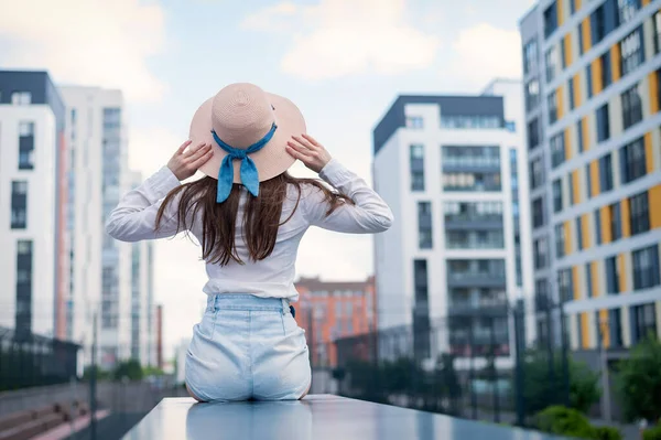 Vista posteriore di una donna con un cappello seduta sullo sfondo della città — Foto Stock