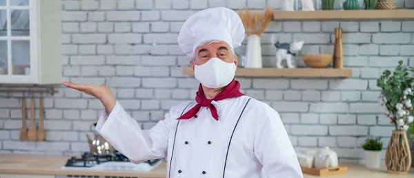 Uomo anziano chef in una maschera medica in una cucina ristorante — Foto Stock