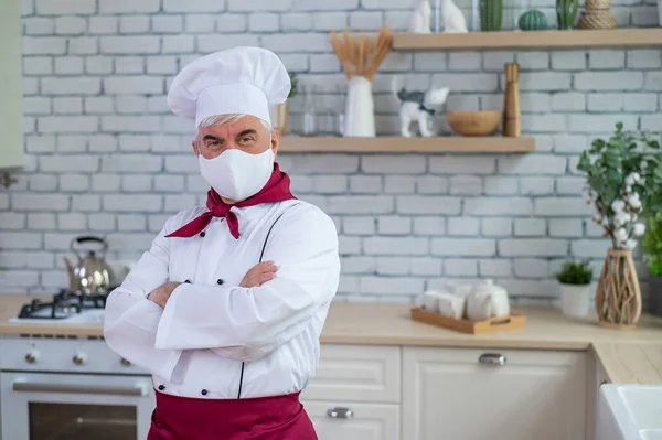 Mutfakta maske takan yaşlı bir erkek şef kollarını göğsünde kavuşturdu. — Stok fotoğraf