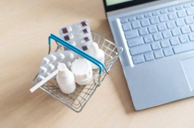 Laptopun yanındaki mini sepetteki ilaçlar. Çevrimiçi eczane kavramı