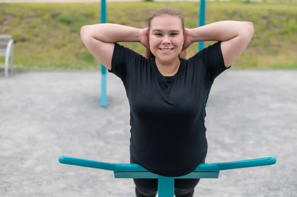 Dicke junge Frau macht Rückenstreckgymnastik an Trainingsgeräten auf dem Sportplatz. — Stockfoto