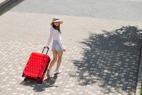 Kaukasische Frau läuft mit rotem Koffer die Straße entlang. — Stockfoto