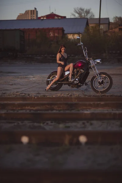 Hermosa mujer sexy en traje de encaje y tacones altos se sienta en una motocicleta en un fondo industrial —  Fotos de Stock
