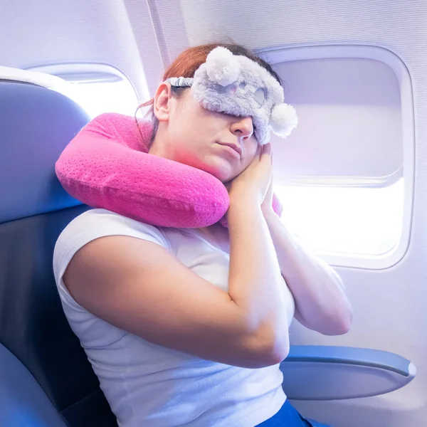 Mujer de pelo rojo cansada durmiendo en el avión con una máscara para los ojos y una almohada para el cuello — Foto de Stock