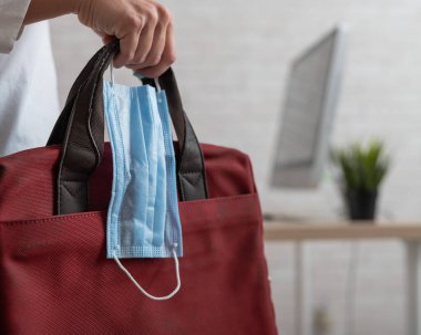 İş kadını elinde laptop ve sağlık maskesi olan bir çanta tutuyor.