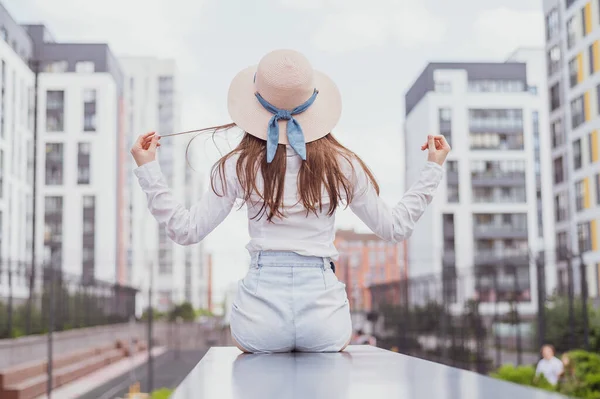 Achteraanzicht van een vrouw in een hoed zittend op de achtergrond van de stad — Stockfoto