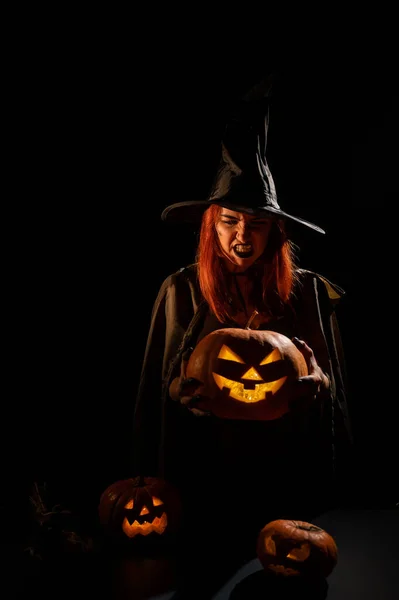 Una bruja malvada sostiene un halloween jack-o-linterna brillando en la oscuridad — Foto de Stock