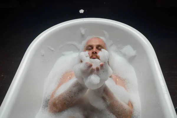 Vista superior de un hombre calvo con una barba roja salpicando en el baño de espuma. Foto humorística. Una parodia de chicas glamorosas. — Foto de Stock