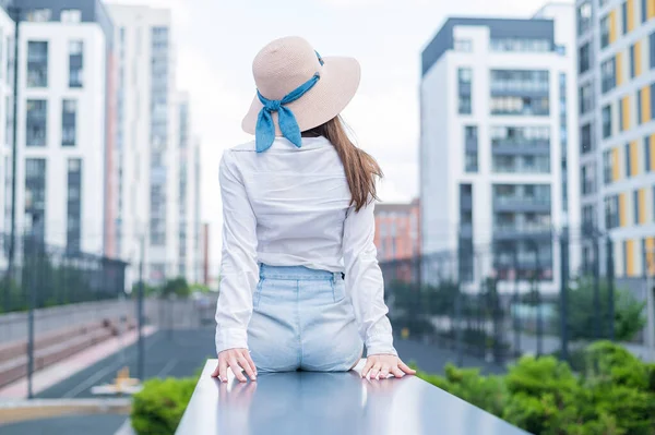 Vista posteriore di una donna con un cappello seduta sullo sfondo della città — Foto Stock