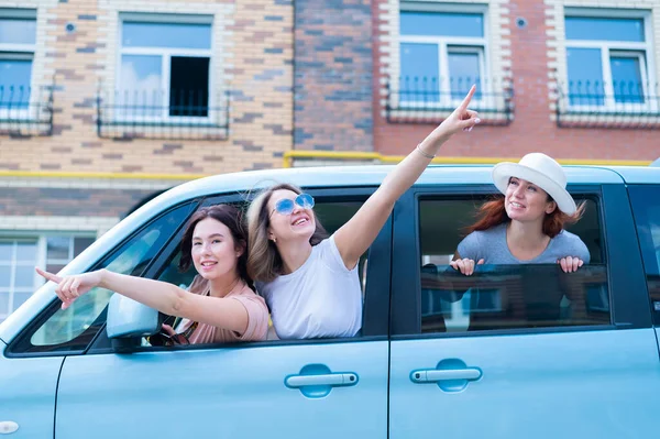 Drei fröhliche kaukasische Freundinnen blicken aus dem Autofenster. Aufgeregte Frauen gehen auf Roadtrip. Die brünette Blondine und der Rotschopf machen Urlaub. — Stockfoto