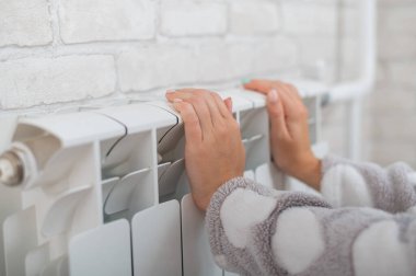 Pijama giyen bir kadın ısıtıcının üzerinde soğuk ellerini ısıtır.