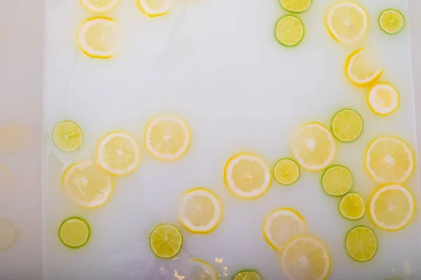 Turbid soapy water in the bath with slices of lemon and lime top view in full frame. Citrus. Spa with milk in the bath for rejuvenation. — Stock Photo, Image