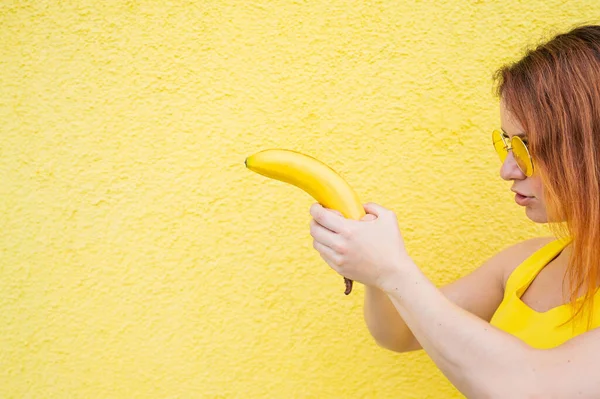 Červenovlasá žena držící banán zobrazující výstřel z pistole — Stock fotografie