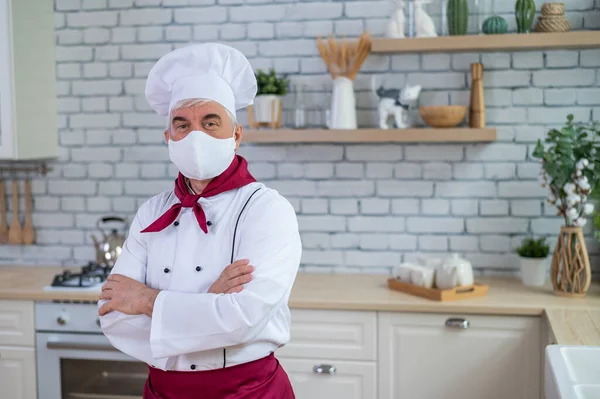 Un cuisinier âgé portant un masque dans la cuisine croise les bras sur la poitrine — Photo