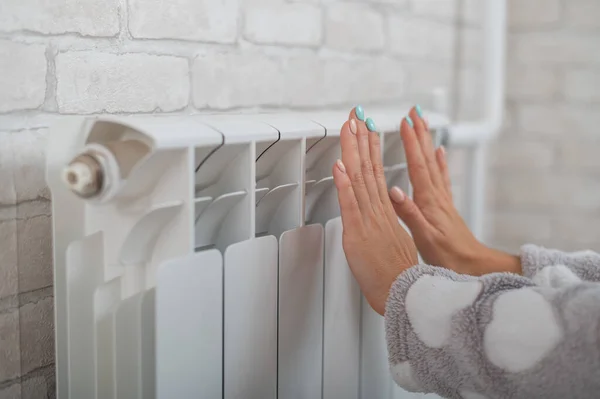 Žena v pyžamu zahřívá studené ruce na topném radiátoru — Stock fotografie