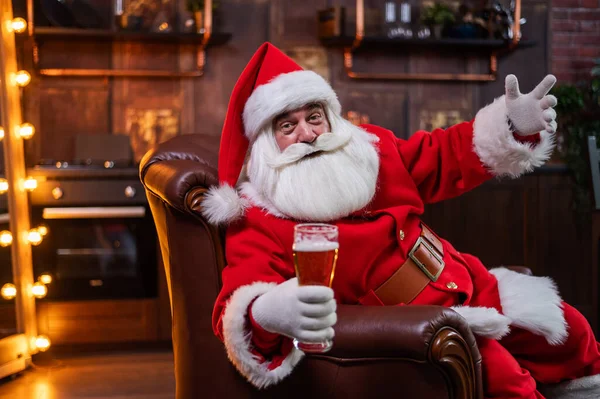 Santa Claus bebe cerveza mientras está sentado en un sillón de cuero — Foto de Stock