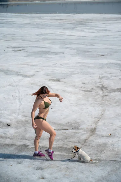 Uma mulher ruiva de biquíni caminha com um cachorro em uma praia nevada — Fotografia de Stock