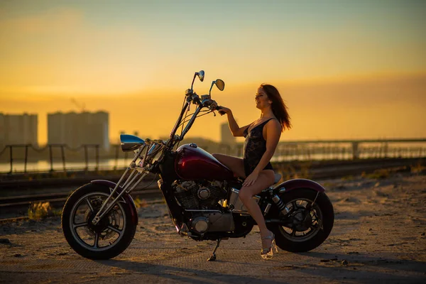 하이힐을 신고 섹시 한 란제리를 입은 빨간 머리 여자가 오토바이에 앉아 있습니다. 노을에 오토바이타고 있는 매력적 인 빨간 머리 소녀 — 스톡 사진