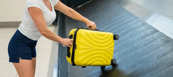 Una mujer sin rostro sacando su maleta amarilla del carrusel de equipaje en la terminal del aeropuerto. — Foto de Stock