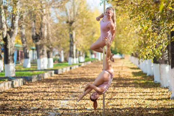 Deux beaux gymnastes font des tours de paire sur une plate-forme portable dans un beau parc d'automne. Deux amis dans le même corps dansent sur une scène de pole portable dans le contexte de la chute des feuilles d'automne. Polonais — Photo