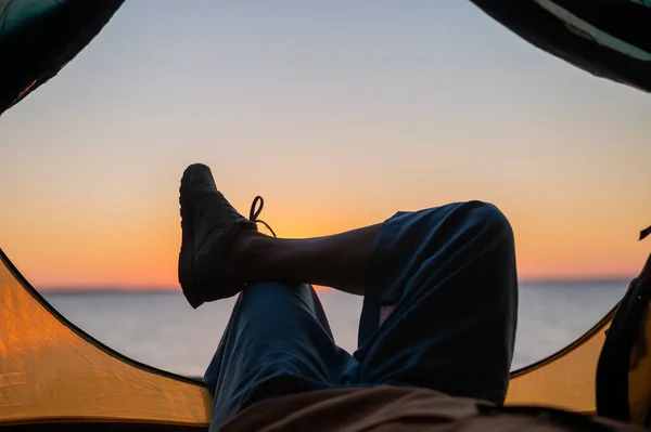 Vue des jambes féminines dans une tente touristique au coucher du soleil sur la plage. La femme fait de la randonnée et campe au bord de la rivière. — Photo