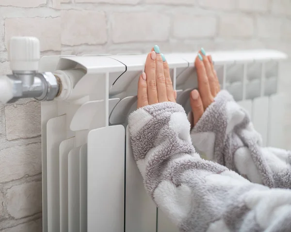 Žena v pyžamu zahřívá studené ruce na topném radiátoru — Stock fotografie
