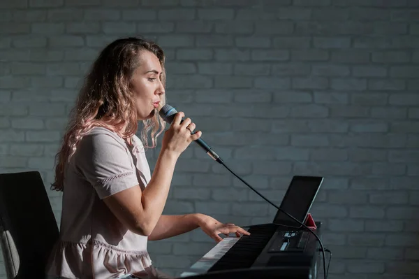 Жінка записує вокальний урок, використовуючи ноутбук і супроводжуючи на клавіатурі під час перебування вдома. Вчитель співає пісню в мікрофон і грає на електронному піаніно. Блогер записує відео . — стокове фото