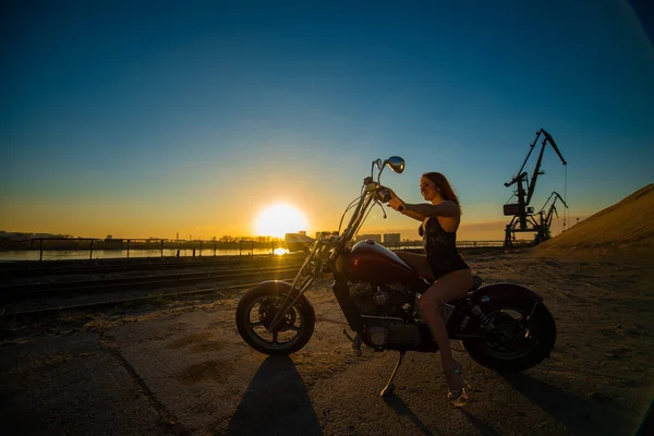 Femme aux cheveux rouges en lingerie sexy en talons hauts s'assoit sur une moto. Attrayant fille aux cheveux roux assis sur une moto au coucher du soleil — Photo