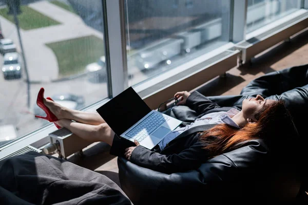 Caucasian woman fell asleep while sitting on bean bag and working on laptop in modern office