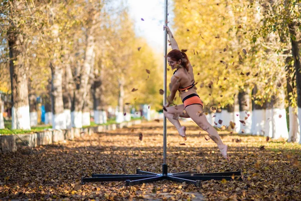 Belle gymnaste faire des tours sur une plate-forme portable dans un beau parc d'automne. femme danse sur une scène de poteau portable sur fond de chute de feuilles d'automne. Pole dance. Une danse étonnante — Photo