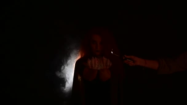 Une sorcière aux longs cheveux bouclés tient un feu magique. Langues de flamme sur les paumes d'une femme rousse. — Video