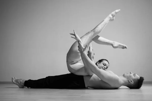 Un dúo de acróbatas mostrando un truco de pareja. Una mujer en un mono de gimnasia con un pie de mano sobre un hombre sin camisa se acuesta boca arriba. Artistas de circo muy flexibles. —  Fotos de Stock