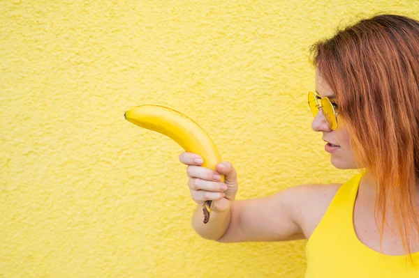 红头发女人拿着一个描绘手枪射击的香蕉 — 图库照片