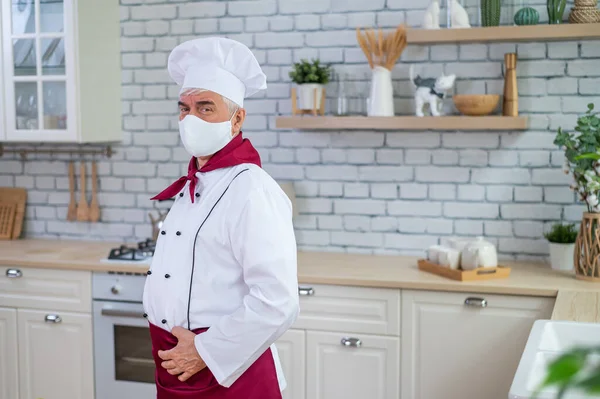 Chef idoso masculino em uma máscara médica em uma cozinha de restaurante — Fotografia de Stock