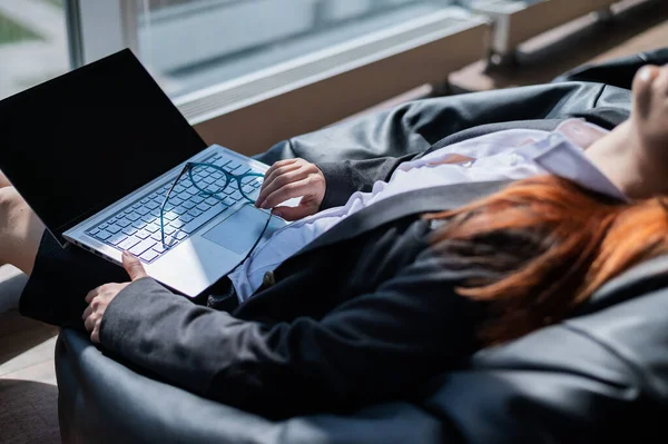 Белая женщина заснула, сидя на бобовом мешке и работая на ноутбуке в современном офисе — стоковое фото