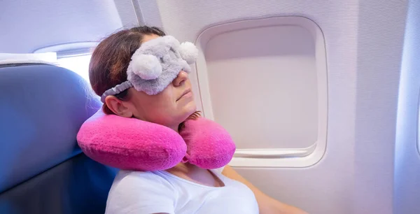 Mujer de pelo rojo cansada durmiendo en el avión con una máscara para los ojos y una almohada para el cuello — Foto de Stock
