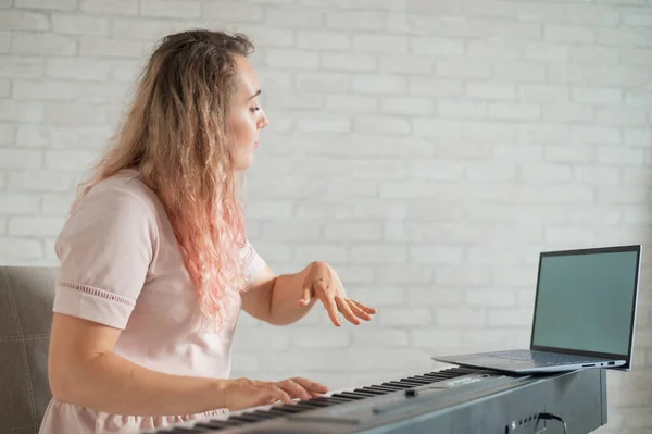 Eine freundliche Frau spielt elektronisches Klavier und führt auf ihrem Laptop einen Videoblog. Bleiben Sie zu Hause. Instrumentallehrer. Musik im Fernstudium unter Quarantäne. — Stockfoto