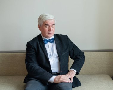 Takım elbiseli, papyonlu ve koltukta oturan kendine güvenen gri saçlı bir iş adamı. Üst düzey erkek patron ofiste..