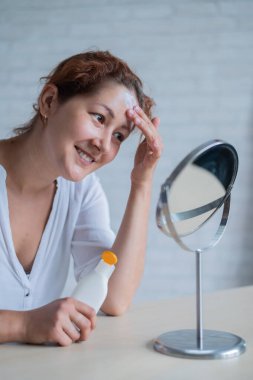 Vitiligo 'su olan beyaz bir kadının portresi güneş kremi kullanıyor. Alnında beyaz pigment lekesi olan bir kız aynaya bakar ve krem sürmüştür..
