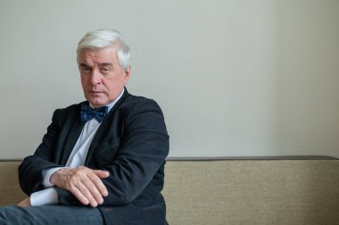 Takım elbiseli, papyonlu ve koltukta oturan kendine güvenen gri saçlı bir iş adamı. Üst düzey erkek patron ofiste..