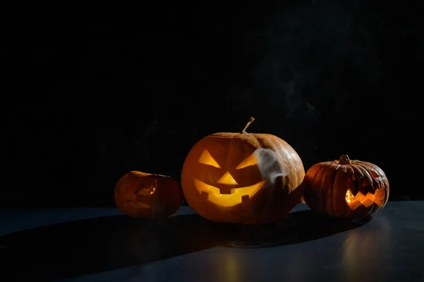 Tarjeta de Halloween. jack o linterna con velas brillan sobre un fondo negro. Una fila de calabazas espeluznantes con muecas talladas fuma en la oscuridad. —  Fotos de Stock