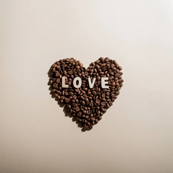 Kalp şeklinde kahve çekirdekleri ve arka planda yazılı aşk. — Stok fotoğraf