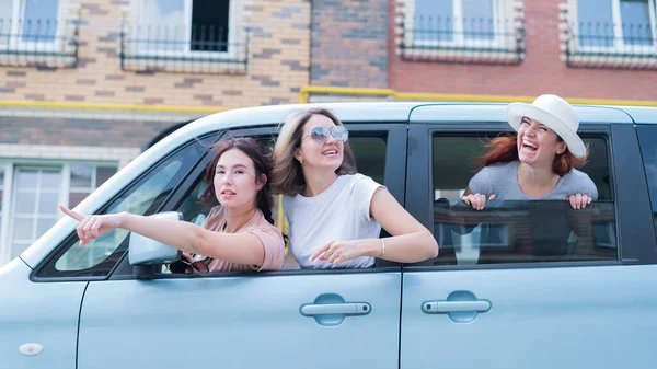 Три радісні кавказькі дівчини дивляться у вікно машини. Задоволені жінки відправляються на дорогу. Бруннетка і руда їдуть у відпустку.. — стокове фото