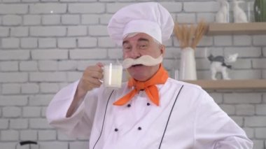 Kalın gri bıyıklı yaşlı bir sütçü bardaktan süt içer.