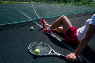 Spor etekli yüzü olmayan bir kız tenis kortunda oturuyor ve elinde bir roket tutuyor. Kadın bacaklarının üst görüntüsü.