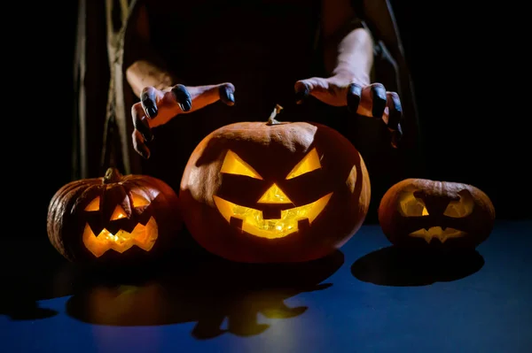 Zbliżenie żeńskich dłoni na dyni na Halloween w ciemnym studio. Czarownica trzyma latarnię. — Zdjęcie stockowe