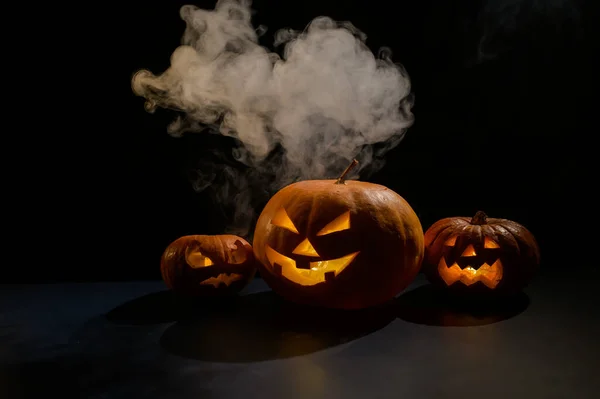 Halloweenkort. jack o lykta med ljus glöd på en svart bakgrund. En rad läskiga pumpor med snidade grimaser röker i mörkret. — Stockfoto