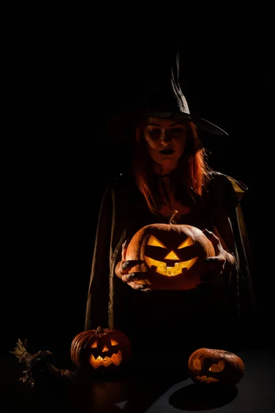 Una bruja malvada sostiene un halloween jack-o-linterna brillando en la oscuridad — Foto de Stock