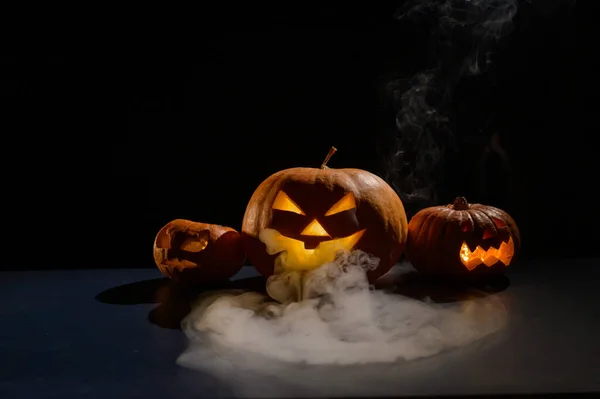 Karta Halloween. Jack o latarnia ze świecami świecą na czarnym tle. Róg przerażających dyń z wyrzeźbionymi grymasami pali w ciemności. — Zdjęcie stockowe